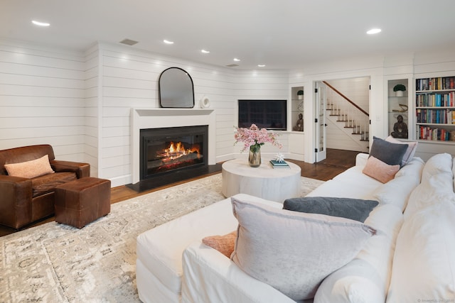living area with stairs, a glass covered fireplace, recessed lighting, and wood finished floors