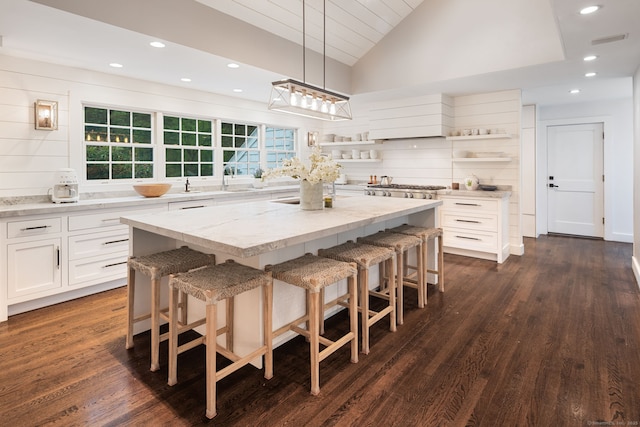 kitchen featuring open shelves, a center island, light stone counters, white cabinets, and vaulted ceiling