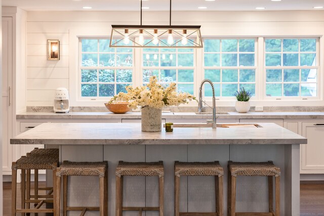 kitchen with a kitchen breakfast bar, white cabinetry, light stone countertops, wood finished floors, and a sink