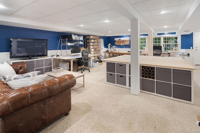 living room featuring carpet floors, a drop ceiling, an office area, and a wainscoted wall