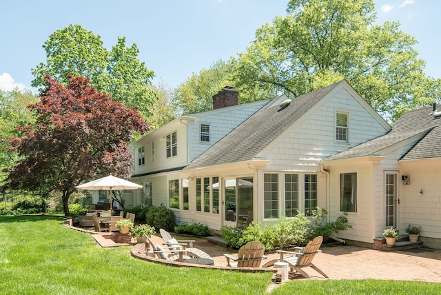 back of property with roof with shingles, a patio, a chimney, and a lawn