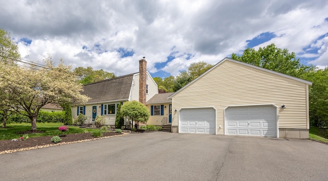 view of front of home featuring roof with shingles, a chimney, driveway, and a garage