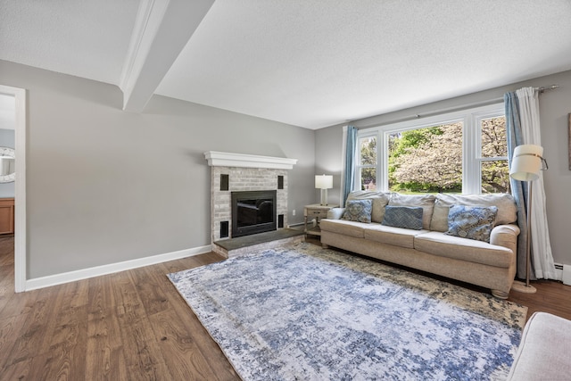 living area with beamed ceiling, wood finished floors, a textured ceiling, baseboards, and a brick fireplace