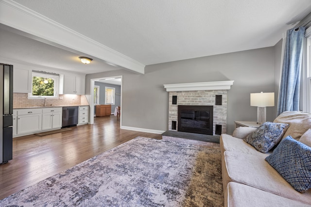 living area with wood finished floors, a brick fireplace, baseboards, and a textured ceiling