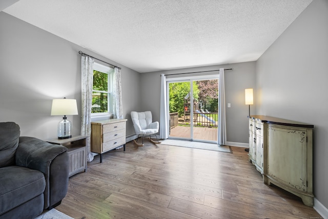 sitting room with wood finished floors, a textured ceiling, a baseboard radiator, and baseboards