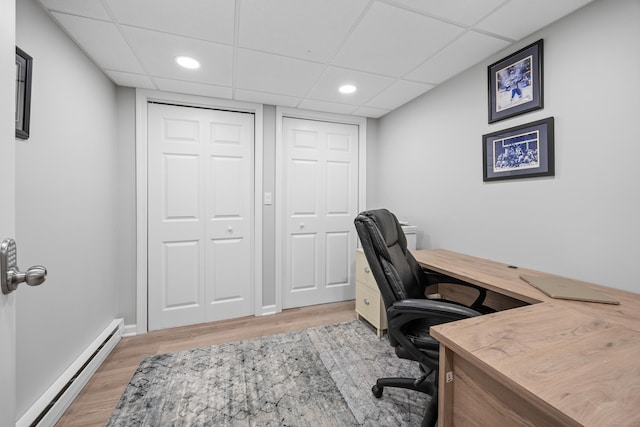 office area featuring baseboard heating, light wood-type flooring, a drop ceiling, and baseboards