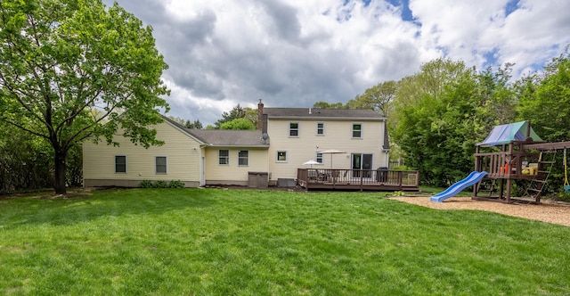 back of house featuring a chimney, a playground, a wooden deck, and a yard