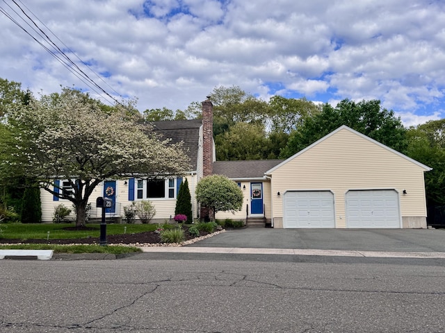 dutch colonial featuring an attached garage, asphalt driveway, a chimney, and a shingled roof