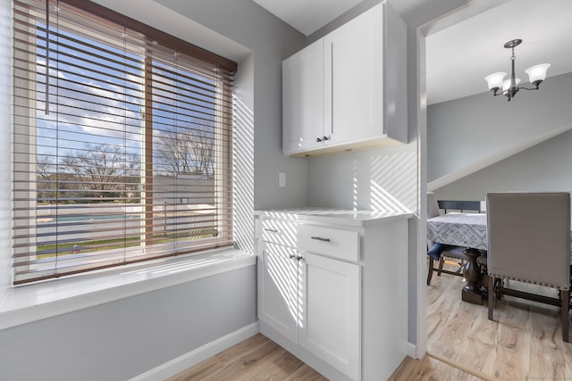 kitchen with baseboards, light wood finished floors, white cabinetry, pendant lighting, and a notable chandelier