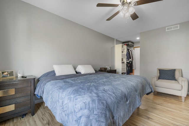 bedroom featuring baseboards, wood finished floors, a walk in closet, visible vents, and a ceiling fan