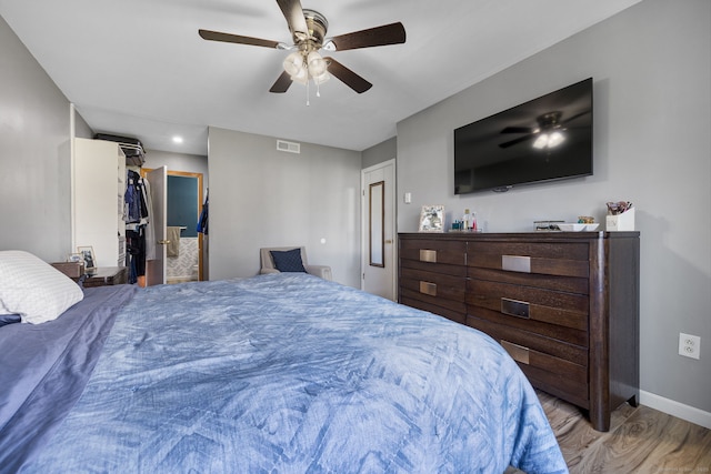 bedroom with wood finished floors, ceiling fan, a walk in closet, baseboards, and visible vents