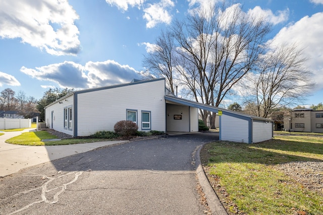 view of front facade featuring a front lawn, an outdoor structure, a carport, aphalt driveway, and fence
