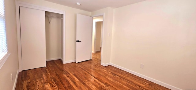 unfurnished bedroom featuring baseboards, wood finished floors, and a closet