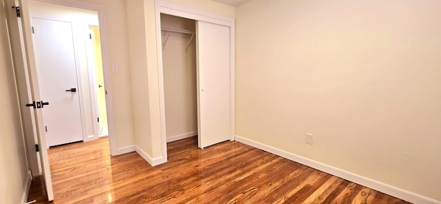 unfurnished bedroom featuring baseboards, wood finished floors, and a closet
