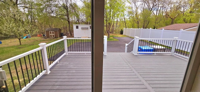 wooden terrace featuring a lawn, an outbuilding, fence, a playground, and a storage unit