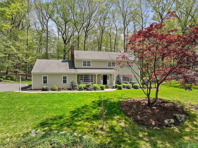 traditional home featuring covered porch, a chimney, and a front lawn