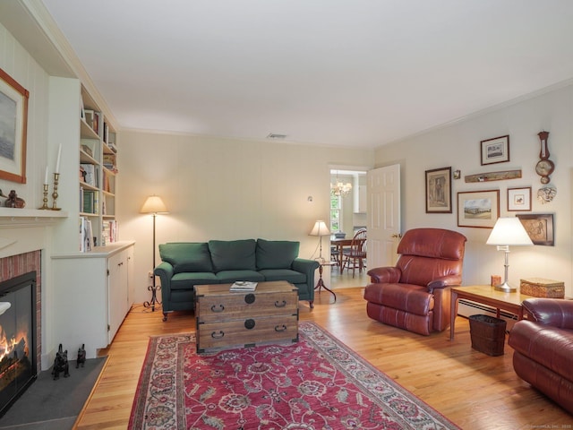 living area with light wood-style flooring, a fireplace, a chandelier, and crown molding