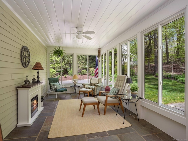 sunroom with plenty of natural light, ceiling fan, and a glass covered fireplace