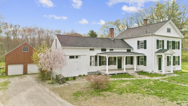 back of house featuring covered porch, a lawn, an outbuilding, a garage, and a shingled roof