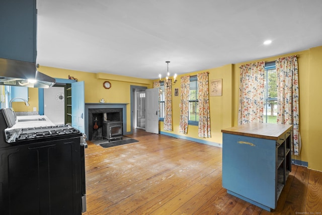 kitchen featuring a wood stove, a chandelier, hardwood / wood-style flooring, a sink, and black gas range oven