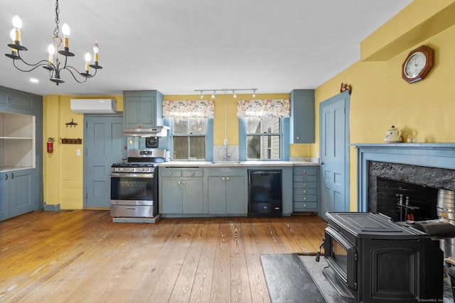 kitchen featuring black dishwasher, stainless steel range with gas cooktop, a wall unit AC, light wood-style flooring, and a notable chandelier