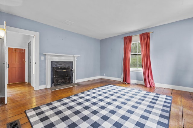 unfurnished living room featuring wood-type flooring, baseboards, visible vents, and a fireplace