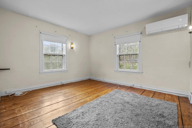 unfurnished room with baseboards, a wall mounted AC, a healthy amount of sunlight, and hardwood / wood-style flooring