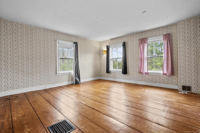 unfurnished room featuring wood-type flooring, baseboards, visible vents, and wallpapered walls