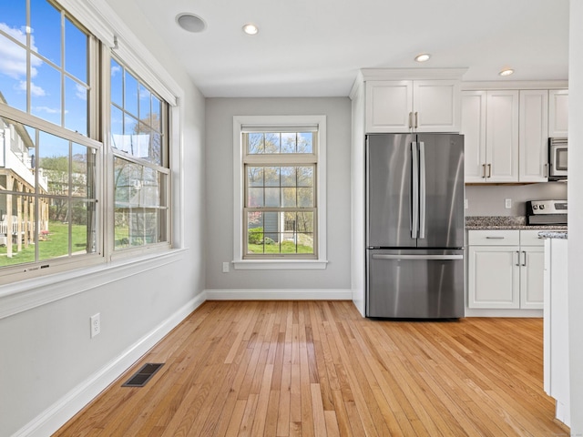 kitchen featuring light wood-style flooring, stainless steel appliances, baseboards, white cabinetry, and visible vents