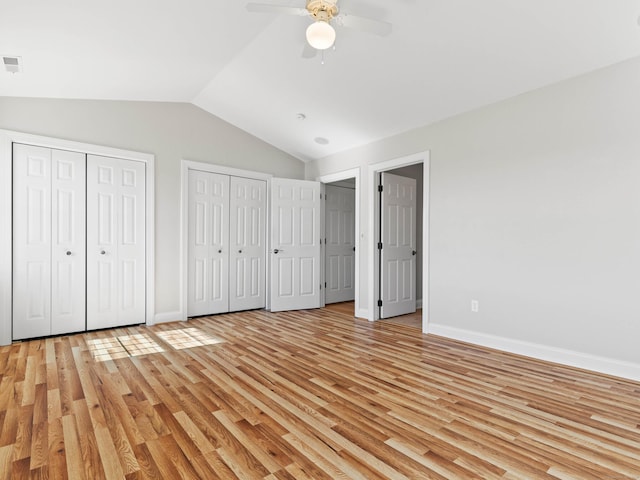 unfurnished bedroom with baseboards, light wood-style flooring, multiple closets, and lofted ceiling