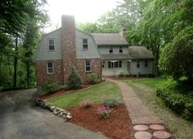 view of front of house with driveway, a chimney, and a gambrel roof