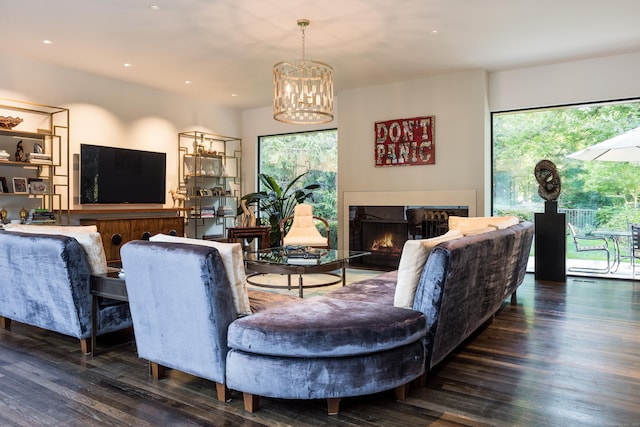 living room featuring a warm lit fireplace, a notable chandelier, wood finished floors, and a healthy amount of sunlight