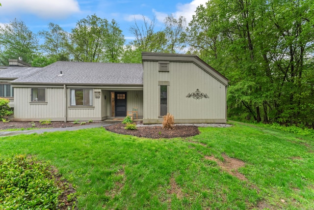 mid-century home with a front lawn, a shingled roof, and a chimney