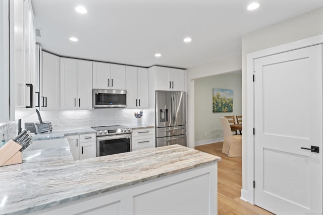 kitchen with stainless steel appliances, a peninsula, recessed lighting, white cabinetry, and light stone countertops