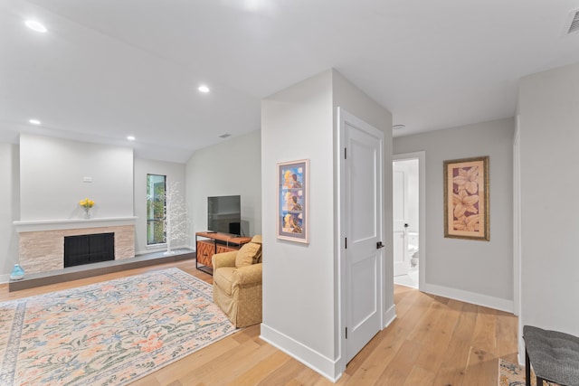 living area featuring light wood-style floors, baseboards, recessed lighting, and a fireplace with raised hearth