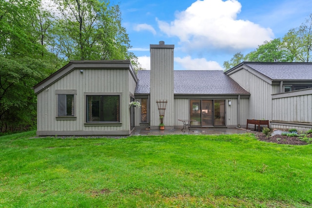 rear view of property with a chimney, a patio area, a lawn, and a shingled roof