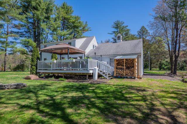 back of house featuring a chimney, roof with shingles, a deck, a gazebo, and a yard