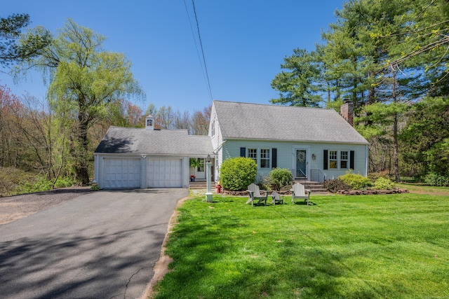 cape cod-style house featuring a shingled roof, an attached garage, a front yard, a chimney, and driveway