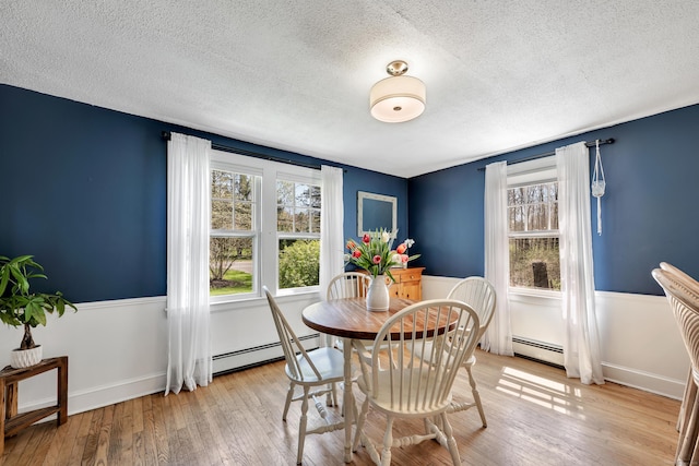 dining area featuring a baseboard radiator, light wood-style flooring, a textured ceiling, and a wainscoted wall