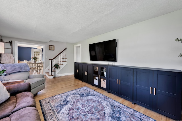 living room with light wood-type flooring, stairs, and a textured ceiling