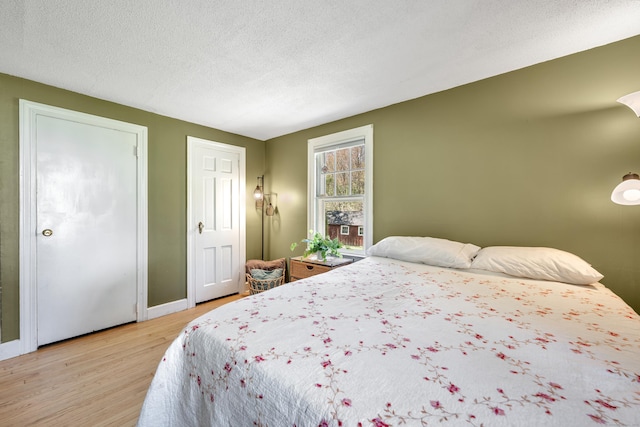 bedroom featuring a textured ceiling, baseboards, and light wood-style floors
