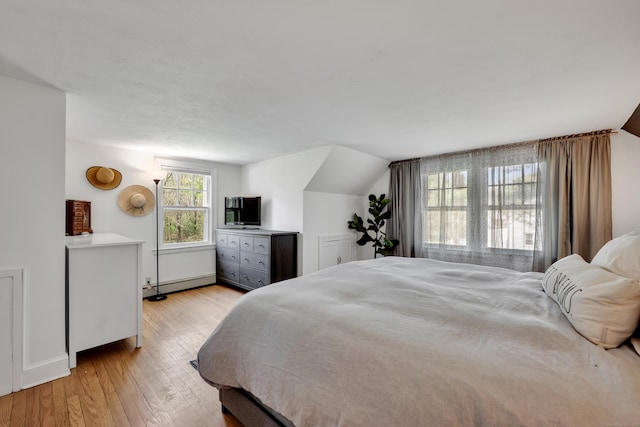 bedroom with a baseboard radiator, vaulted ceiling, and light wood finished floors