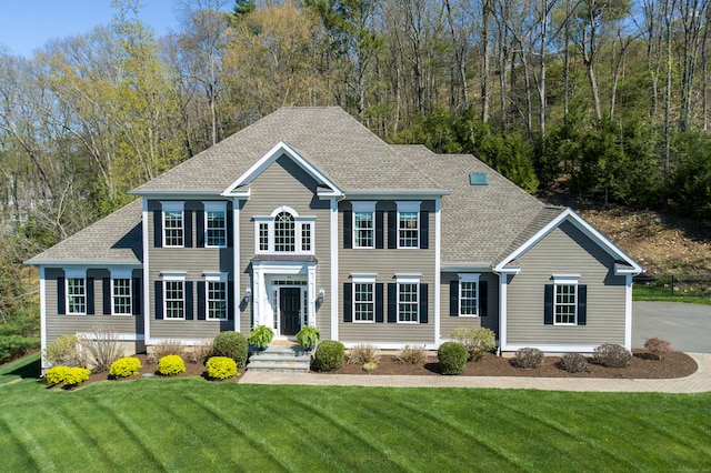 colonial-style house featuring a front yard and roof with shingles