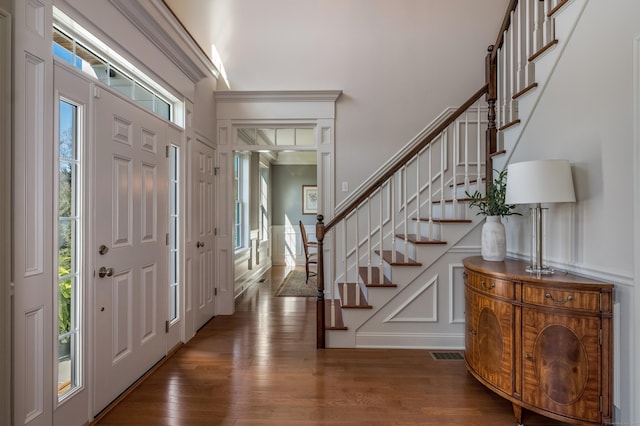 entryway featuring wood finished floors, a decorative wall, visible vents, and stairway