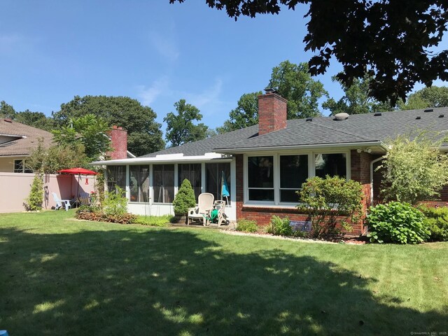 back of house featuring a chimney, a sunroom, brick siding, and a yard