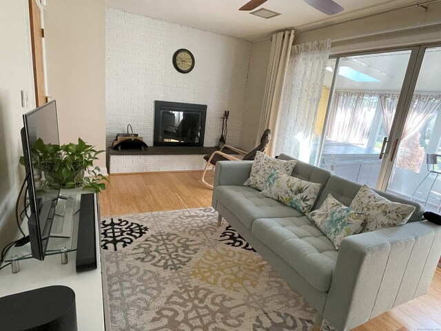 living area with wood finished floors, a brick fireplace, and a ceiling fan