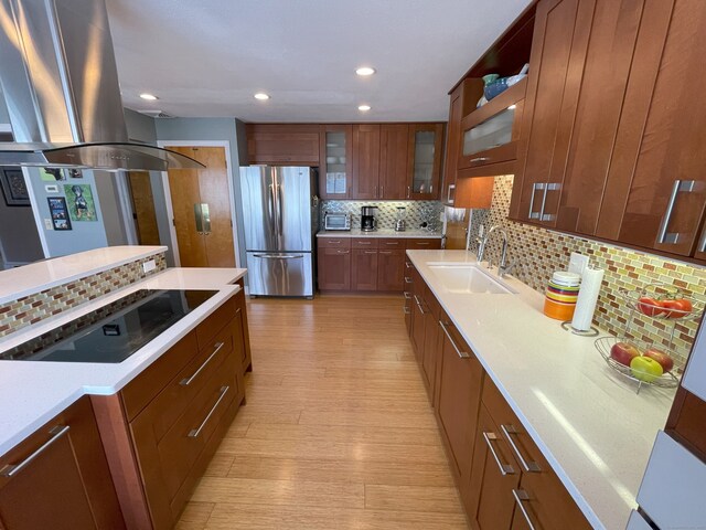 kitchen featuring freestanding refrigerator, a sink, black electric stovetop, island exhaust hood, and backsplash