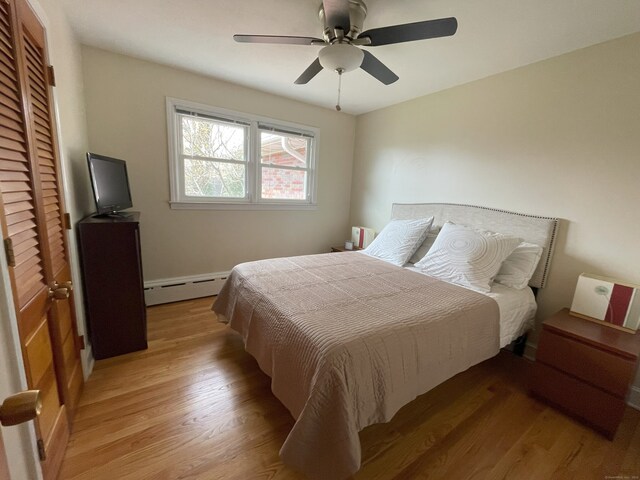 bedroom featuring baseboard heating, light wood-style flooring, a ceiling fan, and a closet