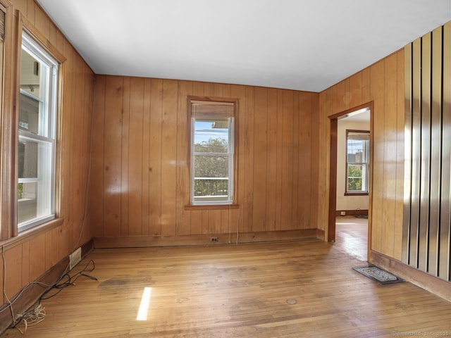 empty room featuring baseboards, light wood-style flooring, and wooden walls