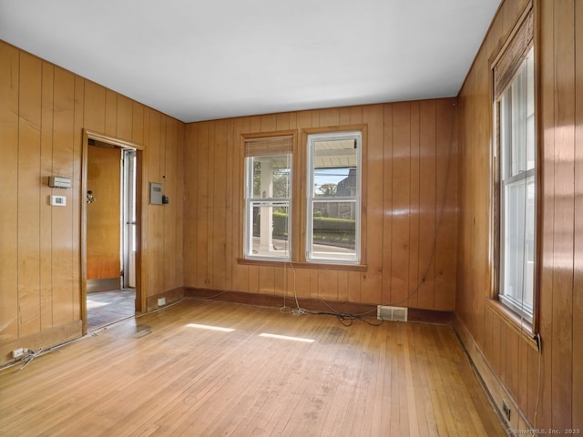 empty room with wood walls, visible vents, and light wood finished floors